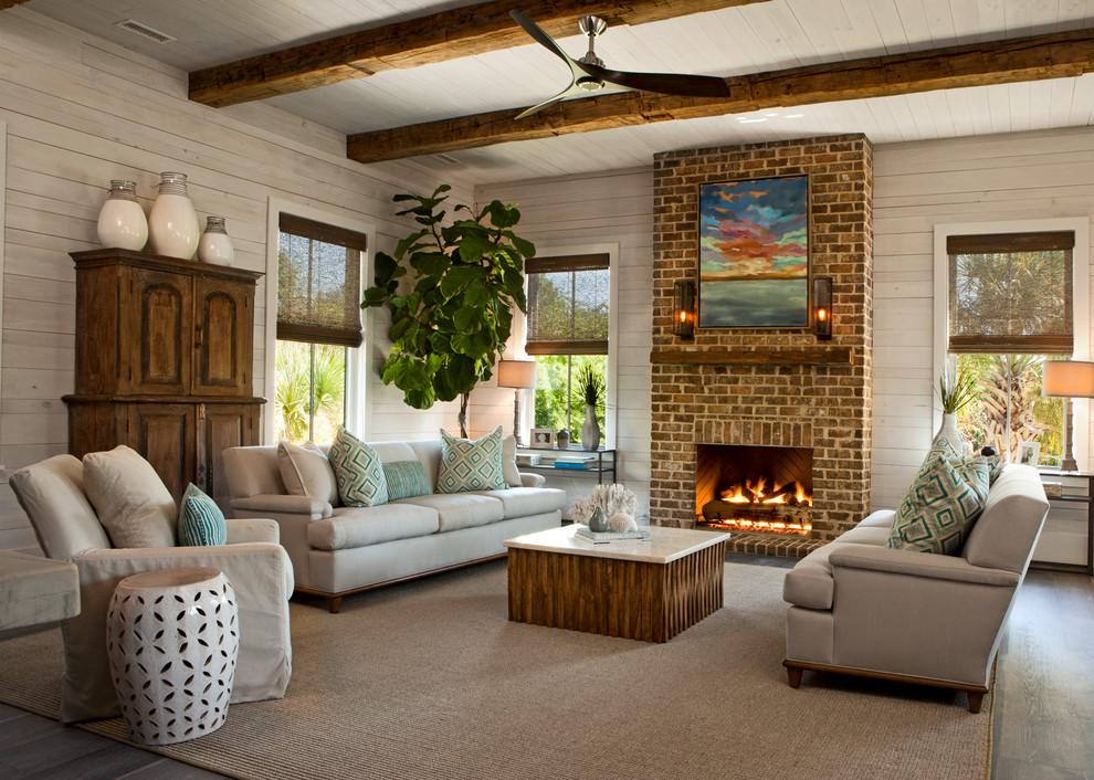 Maritimes Wohnzimmer mit beiger Wandfarbe, dunklem Holzboden, Kamin, Kaminumrandung aus Backstein und grauem Boden in Charleston