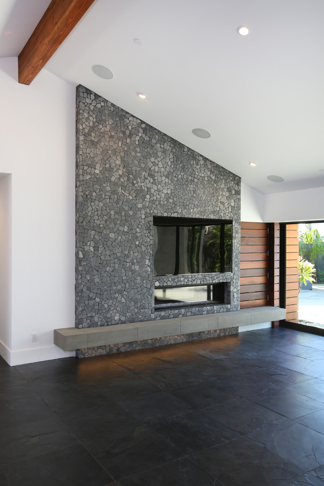 Offenes Modernes Wohnzimmer mit weißer Wandfarbe, Schieferboden, Kamin, Kaminumrandung aus Stein und Multimediawand in Orange County