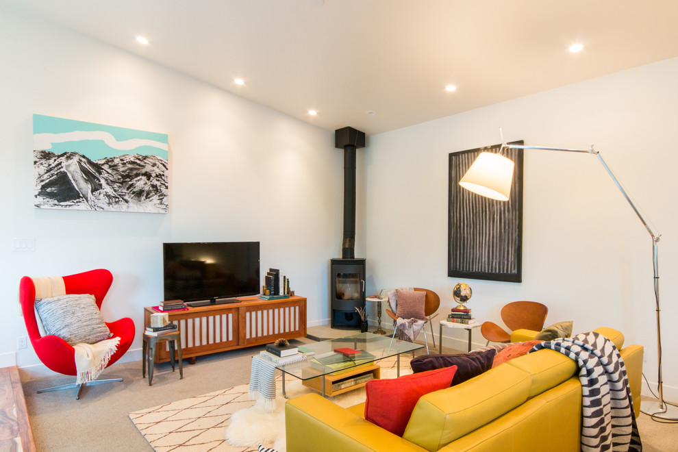 Diseño de salón para visitas abierto retro con paredes blancas, moqueta, estufa de leña, marco de chimenea de metal, televisor independiente y suelo beige