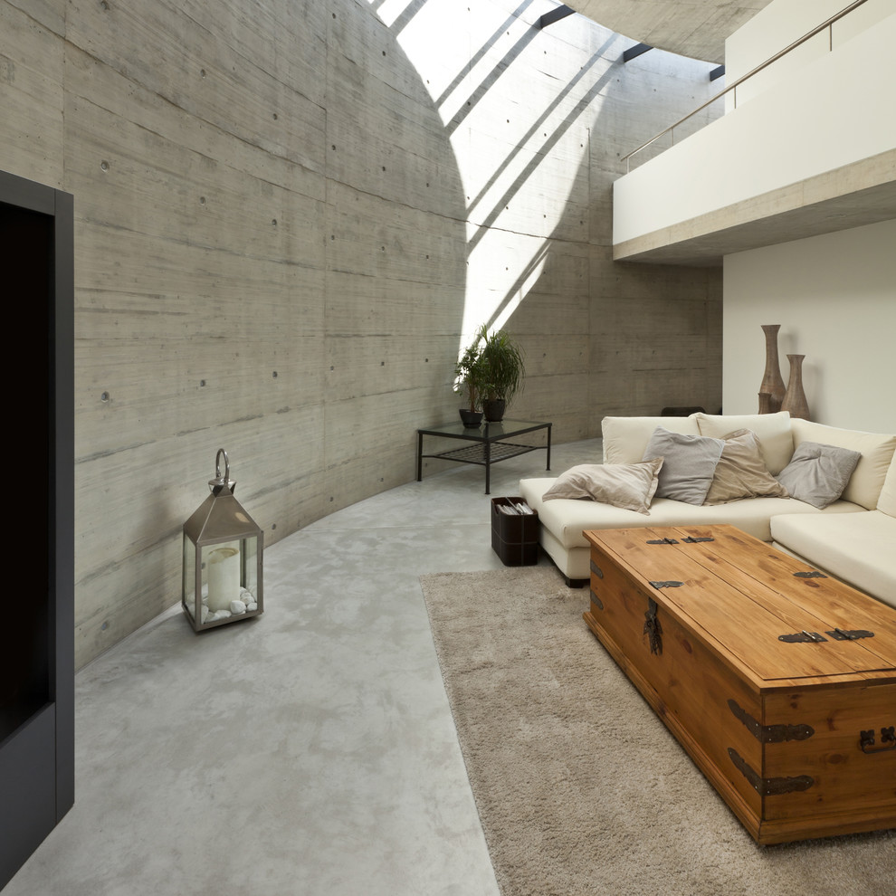Réalisation d'un salon design ouvert avec un mur blanc et sol en béton ciré.