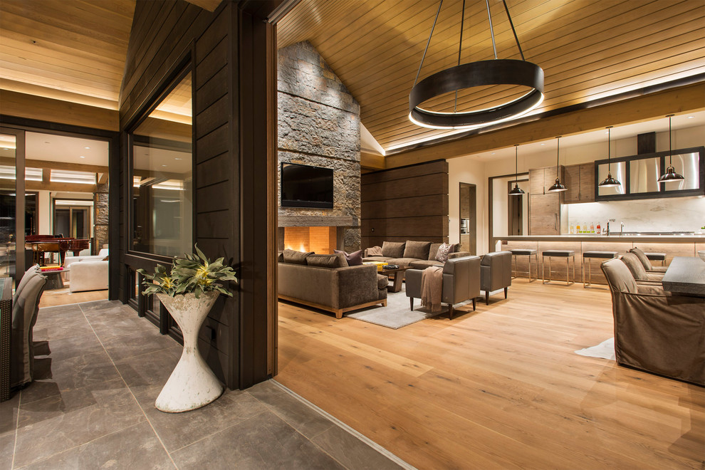 Photo of an expansive modern open plan living room in Denver with beige walls, light hardwood flooring, a standard fireplace, a stone fireplace surround, a wall mounted tv and brown floors.