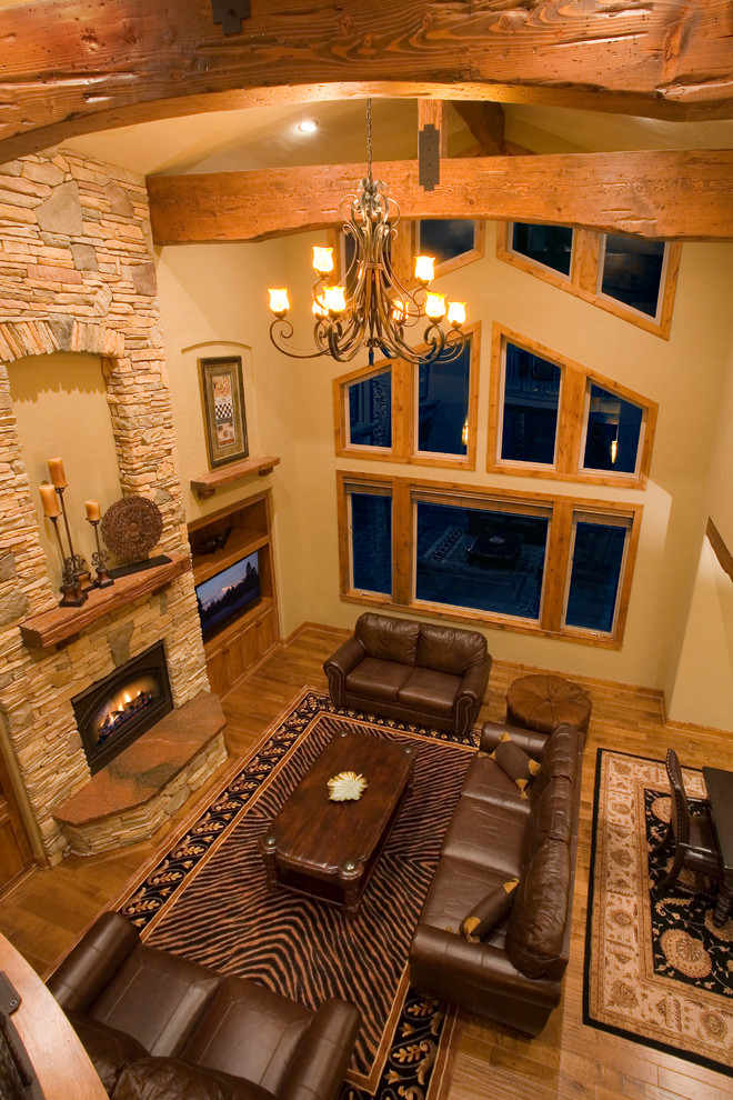Inspiration pour un grand salon chalet ouvert avec un mur beige, un sol en bois brun, une cheminée standard, un manteau de cheminée en pierre et un téléviseur encastré.