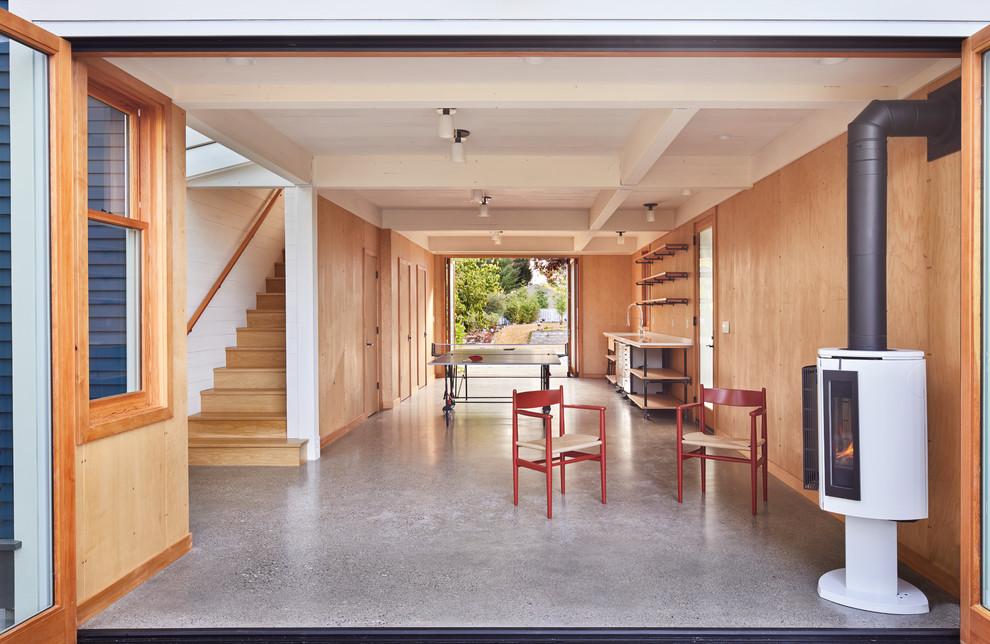 Идея дизайна: маленькая открытая гостиная комната в современном стиле с бетонным полом, печью-буржуйкой и телевизором на стене для на участке и в саду