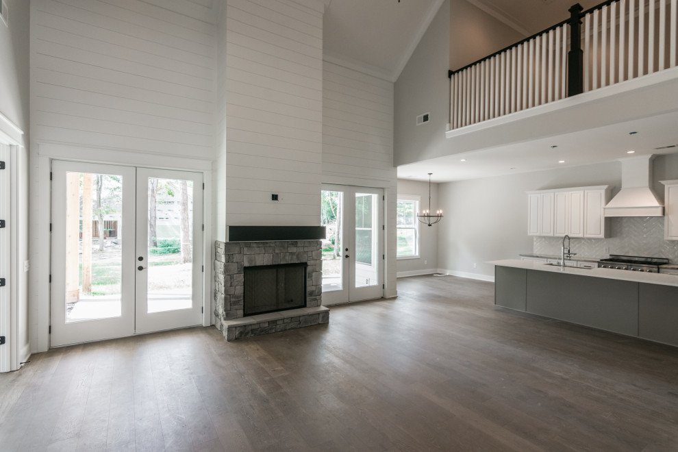 Стильный дизайн: большая открытая гостиная комната в стиле кантри с серыми стенами, полом из винила, стандартным камином, фасадом камина из камня и коричневым полом - последний тренд