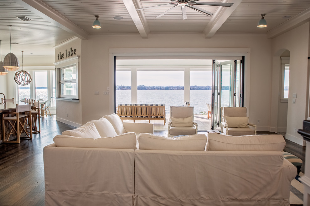 На фото: парадная, открытая гостиная комната среднего размера в морском стиле с белыми стенами, темным паркетным полом, горизонтальным камином, фасадом камина из дерева, скрытым телевизором и коричневым полом