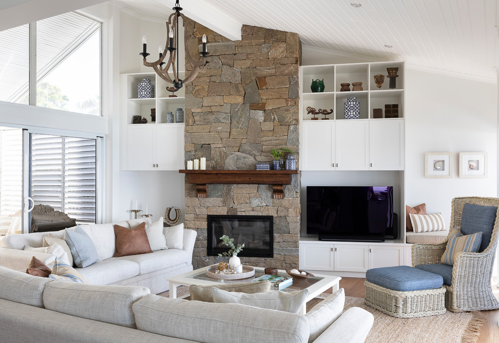 Cette photo montre un grand salon exotique ouvert avec un mur blanc, un sol en bois brun, une cheminée standard, un manteau de cheminée en pierre et un téléviseur indépendant.