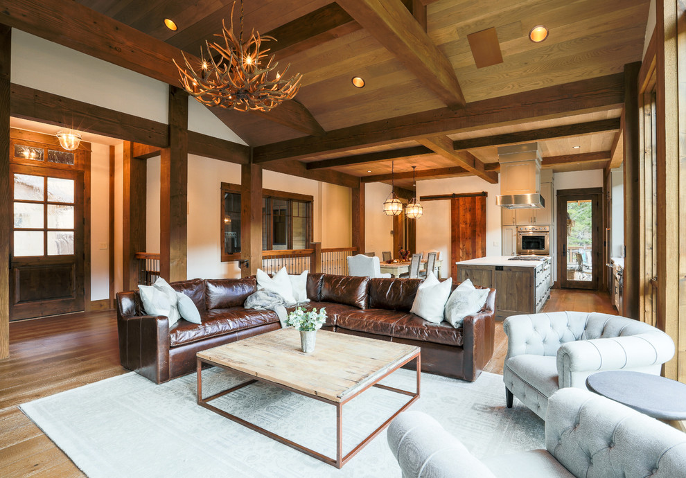 Cette image montre un grand salon chalet ouvert avec une salle de réception, aucun téléviseur, un mur beige, un sol en bois brun et un sol marron.