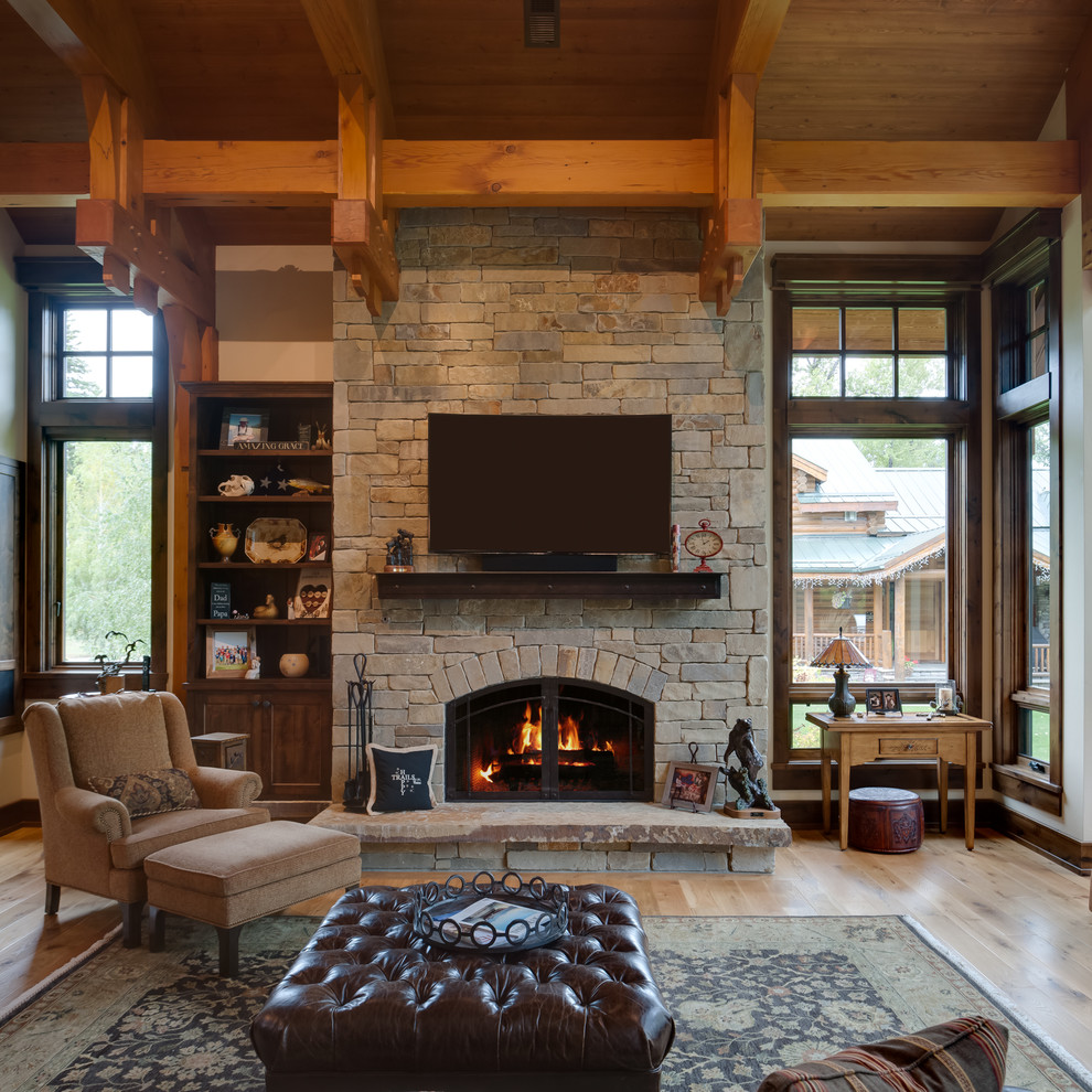 Large mountain style formal and enclosed light wood floor and brown floor living room photo in Other with beige walls, a standard fireplace, a stone fireplace and a wall-mounted tv