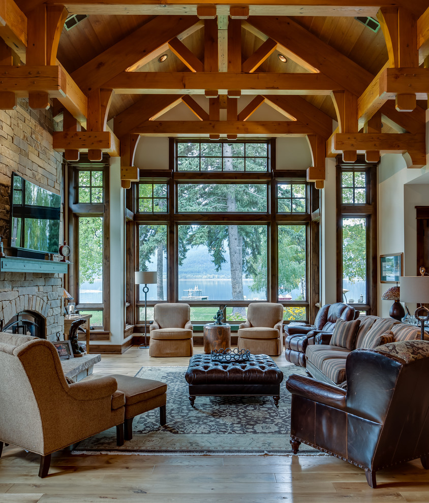 Example of a large mountain style formal and enclosed light wood floor and brown floor living room design in Other with beige walls, a standard fireplace, a stone fireplace and a wall-mounted tv