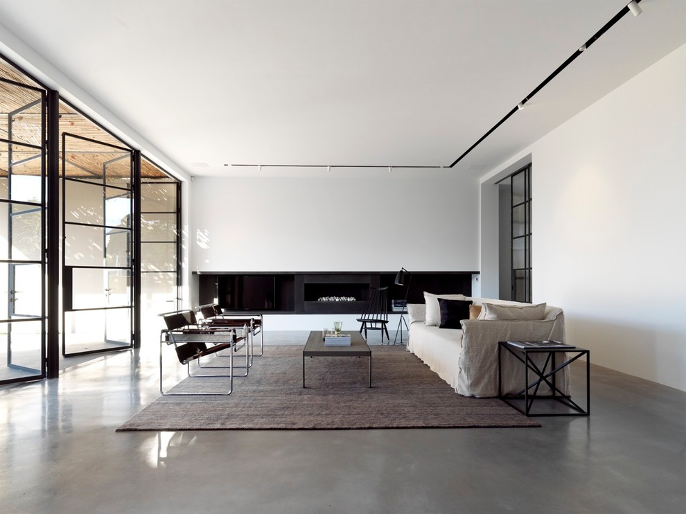 Cette image montre un grand salon minimaliste avec une salle de réception, un mur blanc, sol en béton ciré et une cheminée ribbon.