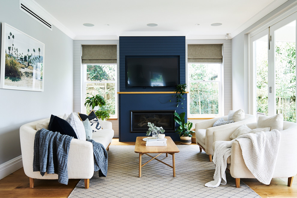 На фото: большая открытая гостиная комната в стиле неоклассика (современная классика) с светлым паркетным полом, горизонтальным камином, телевизором на стене, синими стенами, фасадом камина из металла и коричневым полом с