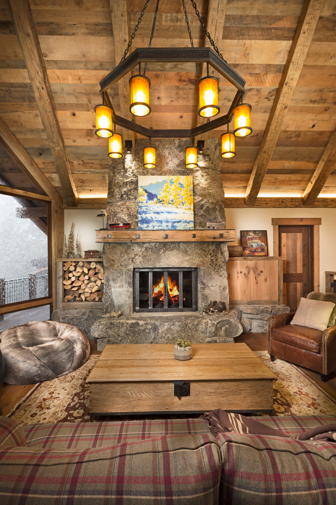 Cette photo montre un grand salon montagne ouvert avec un sol en bois brun, une cheminée standard, un manteau de cheminée en pierre, un téléviseur dissimulé et un mur beige.