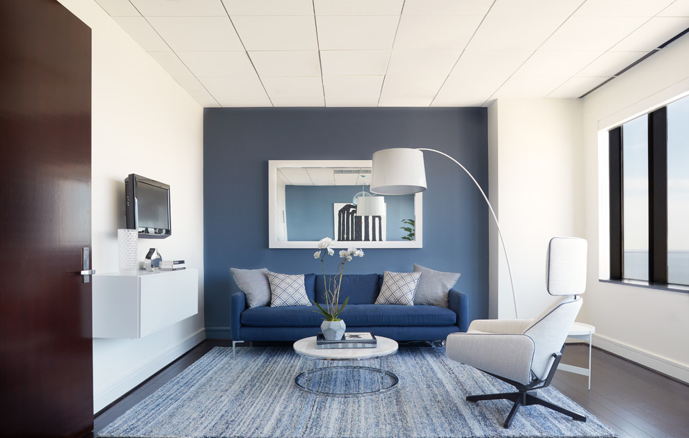 Diseño de salón actual grande con paredes azules, suelo de madera oscura y televisor colgado en la pared