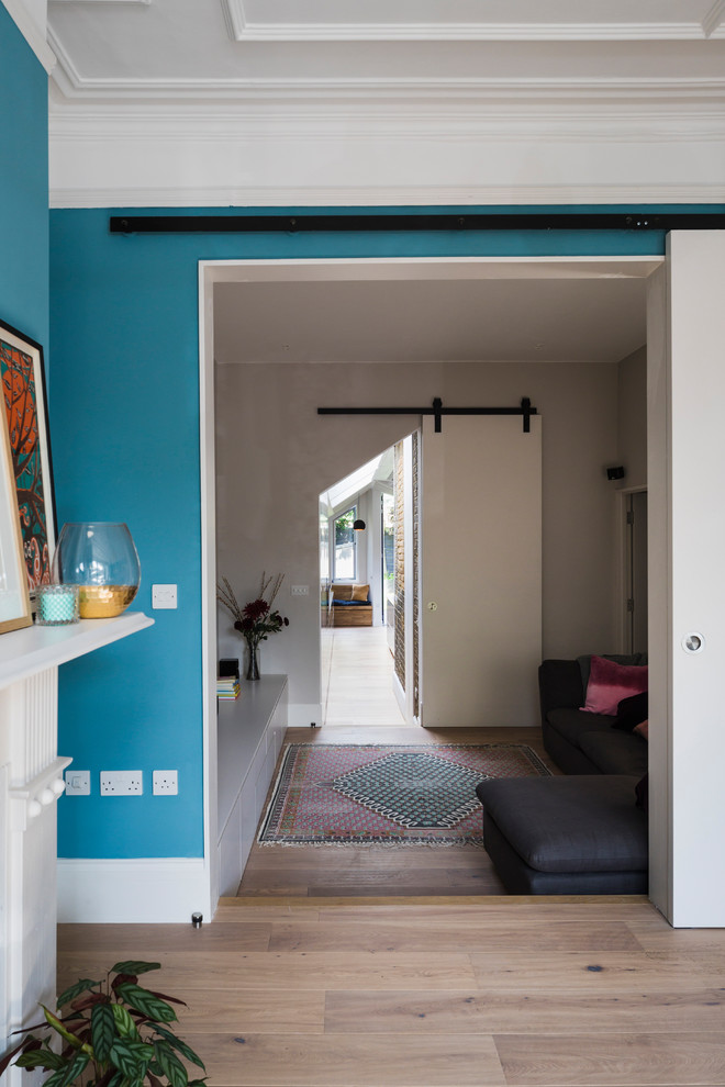 Cette photo montre un salon de taille moyenne avec un mur bleu, parquet clair, une cheminée standard, un manteau de cheminée en bois et un sol marron.
