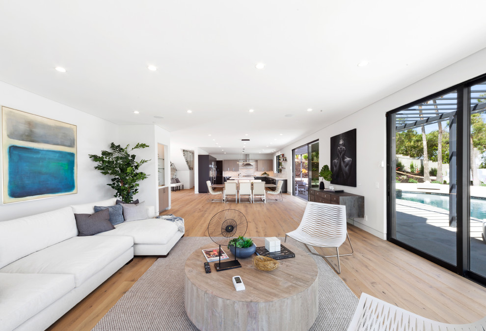 Inspiration for a large contemporary open plan living room in Los Angeles with white walls, light hardwood flooring, a standard fireplace, a plastered fireplace surround and a wall mounted tv.