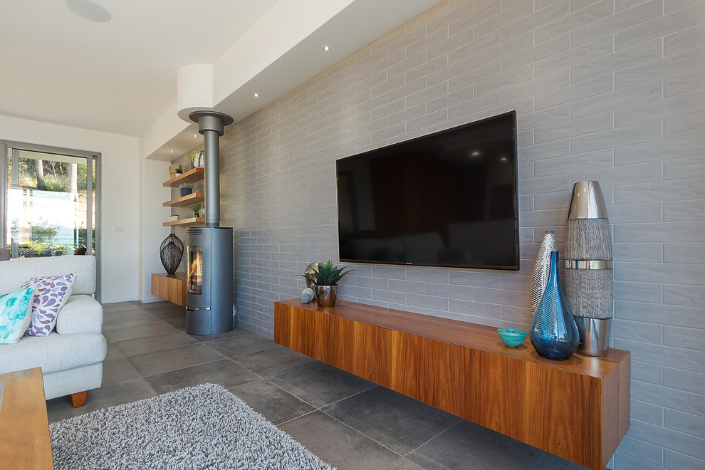 Свежая идея для дизайна: открытая гостиная комната среднего размера в стиле модернизм с серыми стенами, полом из керамической плитки, печью-буржуйкой, фасадом камина из металла и телевизором на стене - отличное фото интерьера