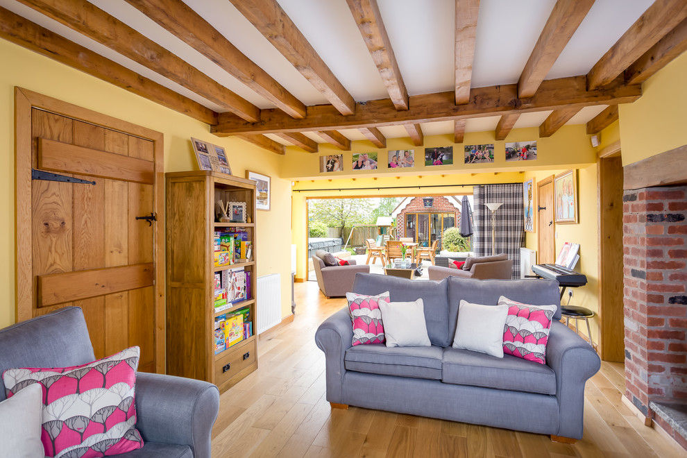 Imagen de salón para visitas abierto de estilo de casa de campo grande con paredes amarillas, suelo laminado, estufa de leña, marco de chimenea de ladrillo y televisor independiente