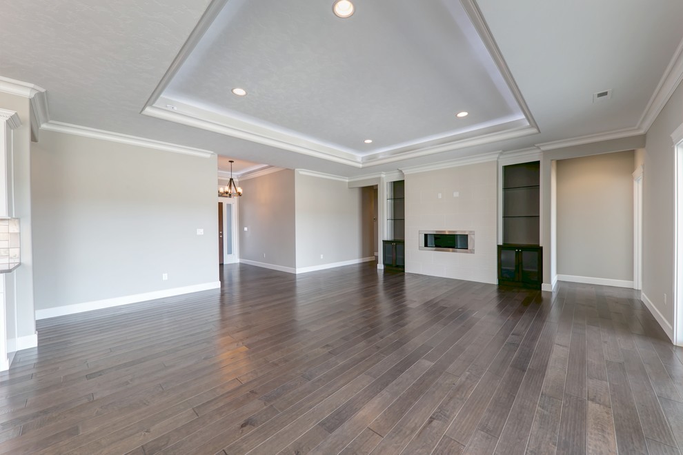 Aménagement d'un grand salon classique ouvert avec un mur gris, un sol en bois brun, une cheminée standard, un manteau de cheminée en carrelage et un téléviseur encastré.