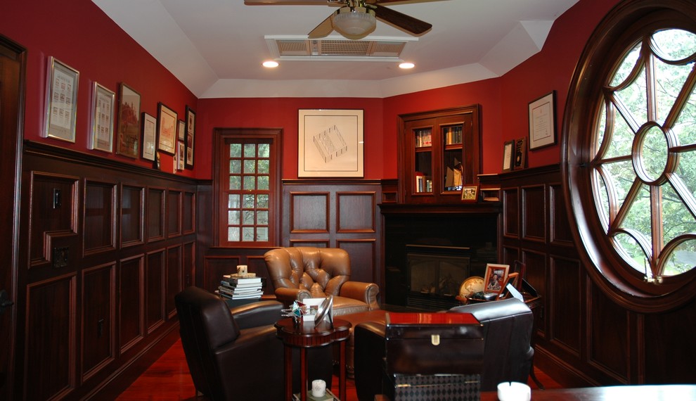 Idée de décoration pour un petit salon tradition fermé avec une bibliothèque ou un coin lecture, un mur rouge, un sol en bois brun, une cheminée d'angle et un manteau de cheminée en bois.
