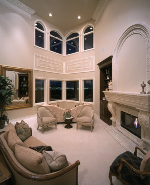 This is an example of an expansive classic formal open plan living room in Las Vegas with beige walls, carpet, a standard fireplace, a concrete fireplace surround, no tv and beige floors.