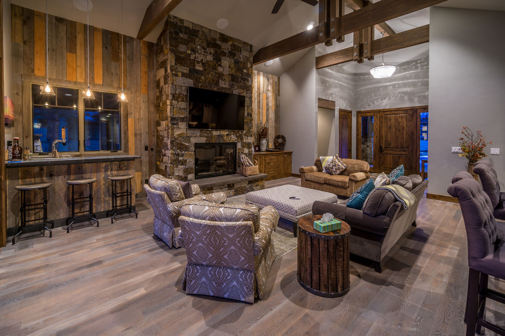 Inspiration for a large rustic open concept medium tone wood floor living room remodel in Other with a bar, gray walls, a standard fireplace, a stone fireplace and a wall-mounted tv