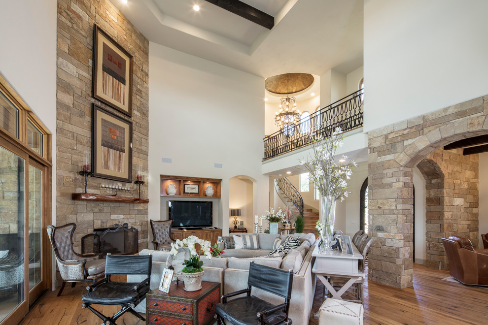 Example of a large tuscan formal and open concept light wood floor living room design in Austin with white walls, a corner fireplace, a stone fireplace and a tv stand