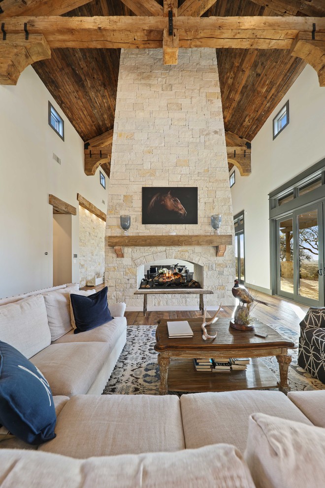 Cette photo montre un salon montagne ouvert avec un mur beige, un sol en bois brun, une cheminée double-face, un manteau de cheminée en pierre et un sol marron.