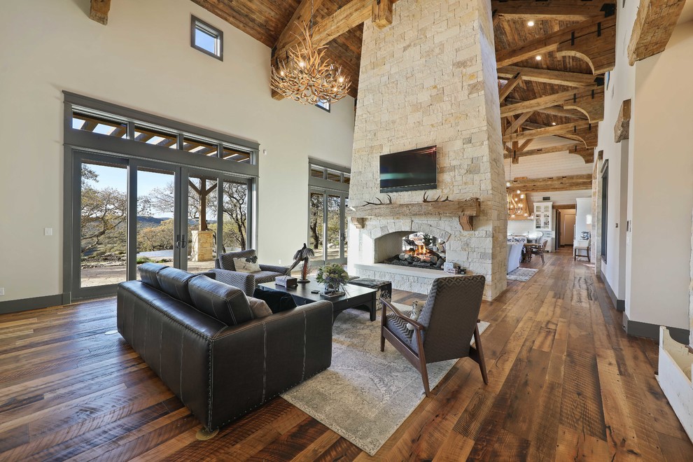 Inspiration for a rustic open concept medium tone wood floor and brown floor living room remodel in Austin with beige walls, a two-sided fireplace, a stone fireplace and a wall-mounted tv