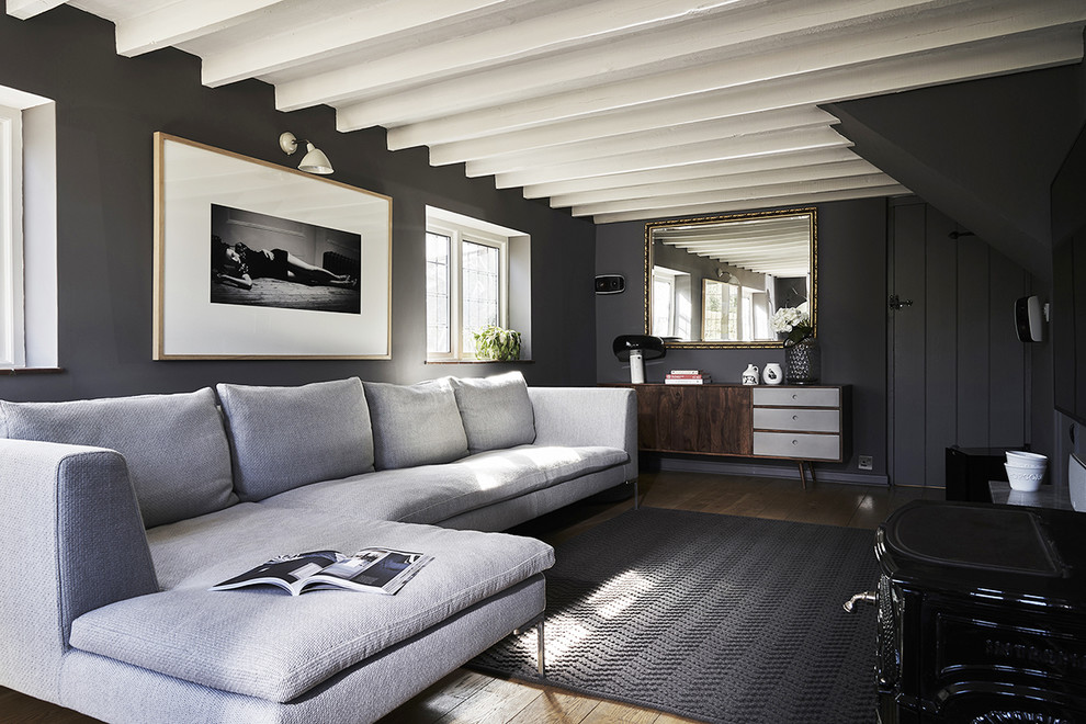 Example of a mid-sized country enclosed medium tone wood floor and brown floor living room library design in Hampshire with gray walls, a wood stove, a stone fireplace and a wall-mounted tv