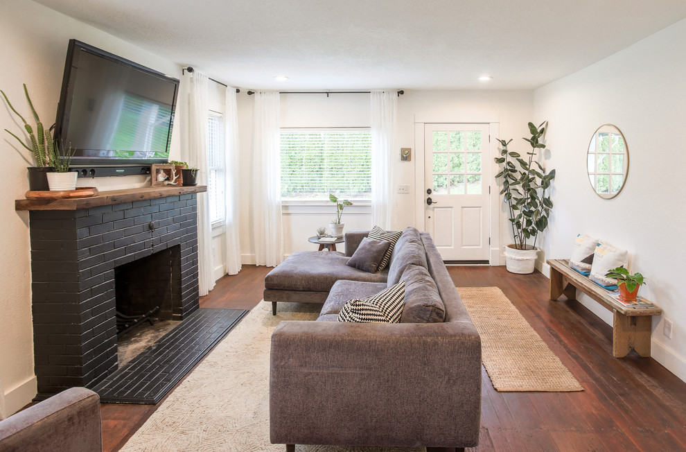 На фото: маленькая открытая гостиная комната в стиле кантри с белыми стенами, паркетным полом среднего тона, стандартным камином, фасадом камина из кирпича, телевизором на стене и коричневым полом для на участке и в саду