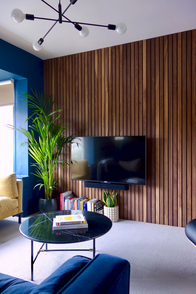 Aménagement d'un grand salon rétro ouvert avec un mur bleu, moquette, un téléviseur fixé au mur et un sol gris.