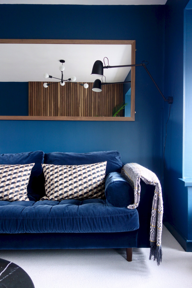 Cette image montre un grand salon vintage ouvert avec un mur bleu, moquette, un téléviseur fixé au mur et un sol gris.