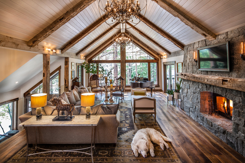 Réalisation d'un grand salon chalet ouvert avec un manteau de cheminée en pierre, un téléviseur fixé au mur, une salle de musique, un mur blanc, parquet foncé, un poêle à bois et un sol marron.