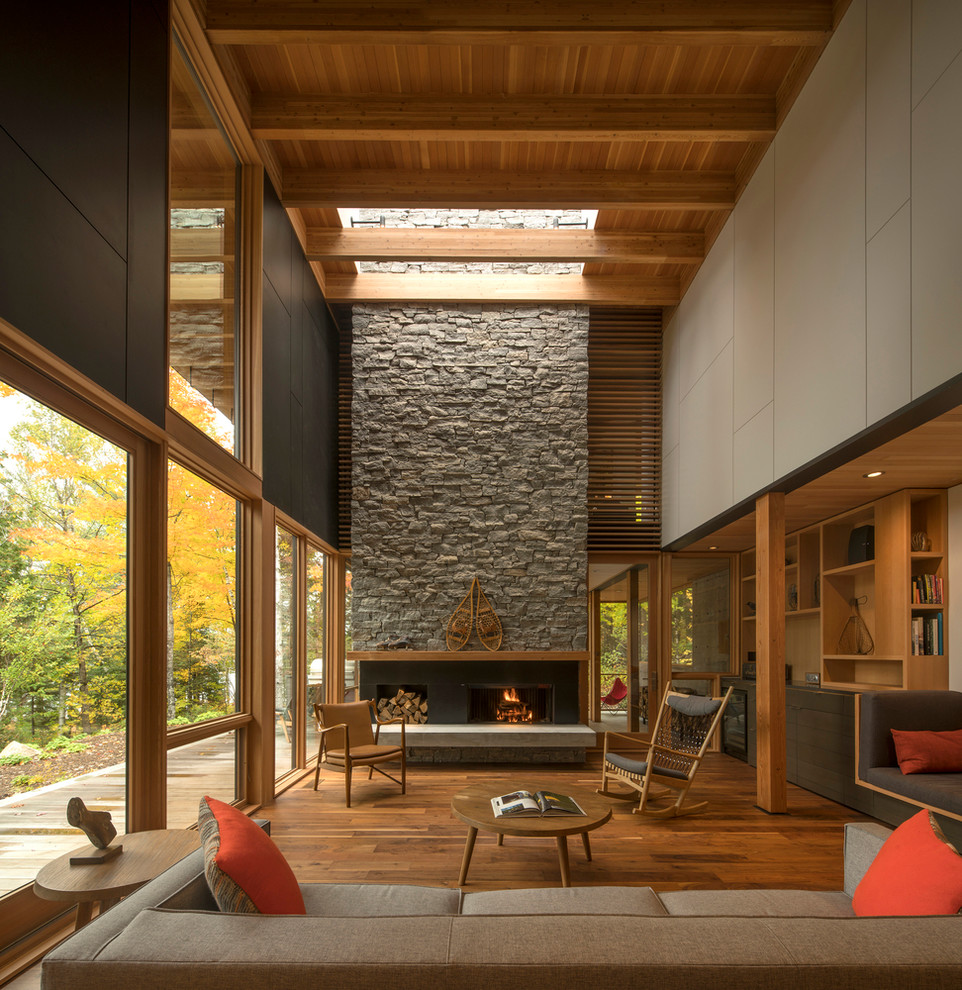 Inspiration pour un salon design de taille moyenne et ouvert avec un sol en bois brun, une cheminée standard, un manteau de cheminée en pierre, aucun téléviseur et un sol marron.