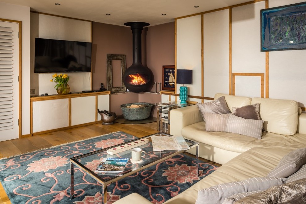 Mid-sized eclectic formal and enclosed medium tone wood floor and brown floor living room photo in Cornwall with multicolored walls, a wood stove, a plaster fireplace and a wall-mounted tv