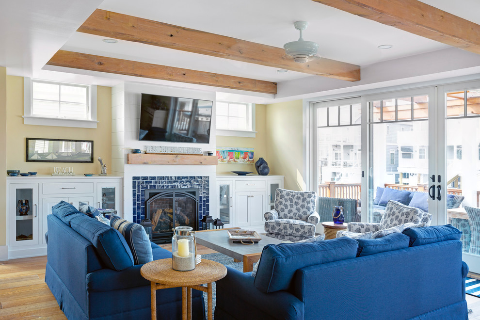 Maritimes Wohnzimmer mit gelber Wandfarbe, braunem Holzboden, Kamin, gefliester Kaminumrandung, TV-Wand und braunem Boden in Sonstige