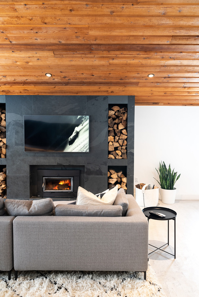 This is an example of a contemporary living room in Toronto with concrete flooring, a wood burning stove, white walls, a tiled fireplace surround, a wall mounted tv and white floors.