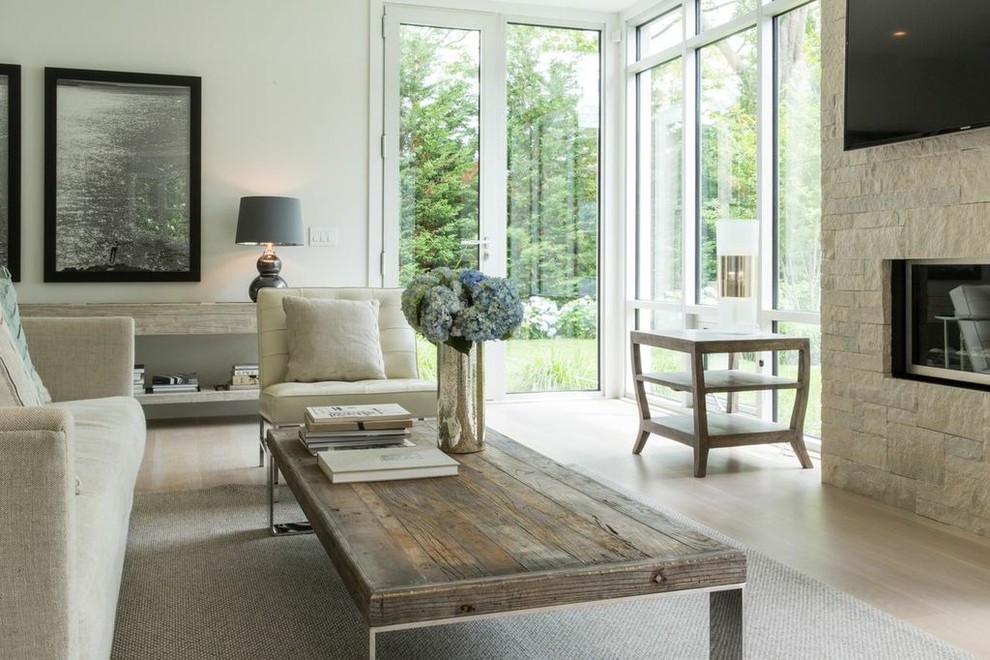 Стильный дизайн: гостиная комната в современном стиле с белыми стенами, фасадом камина из камня и телевизором на стене - последний тренд