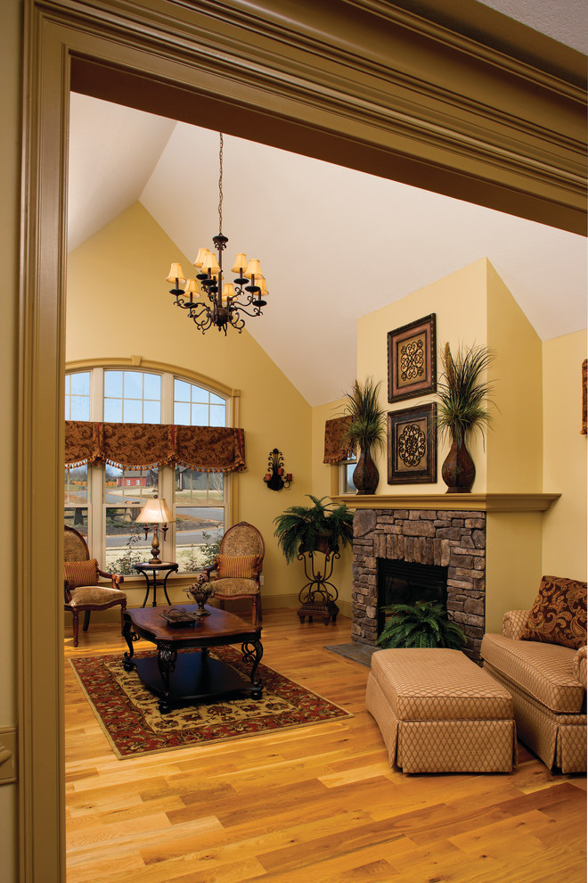 На фото: гостиная комната среднего размера в классическом стиле с желтыми стенами, паркетным полом среднего тона, стандартным камином и фасадом камина из камня без телевизора с
