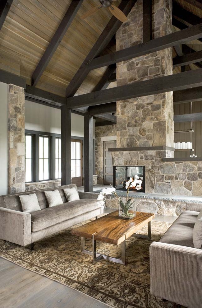 Expansive rustic formal open plan living room in Other with grey walls, light hardwood flooring, a two-sided fireplace and a stone fireplace surround.