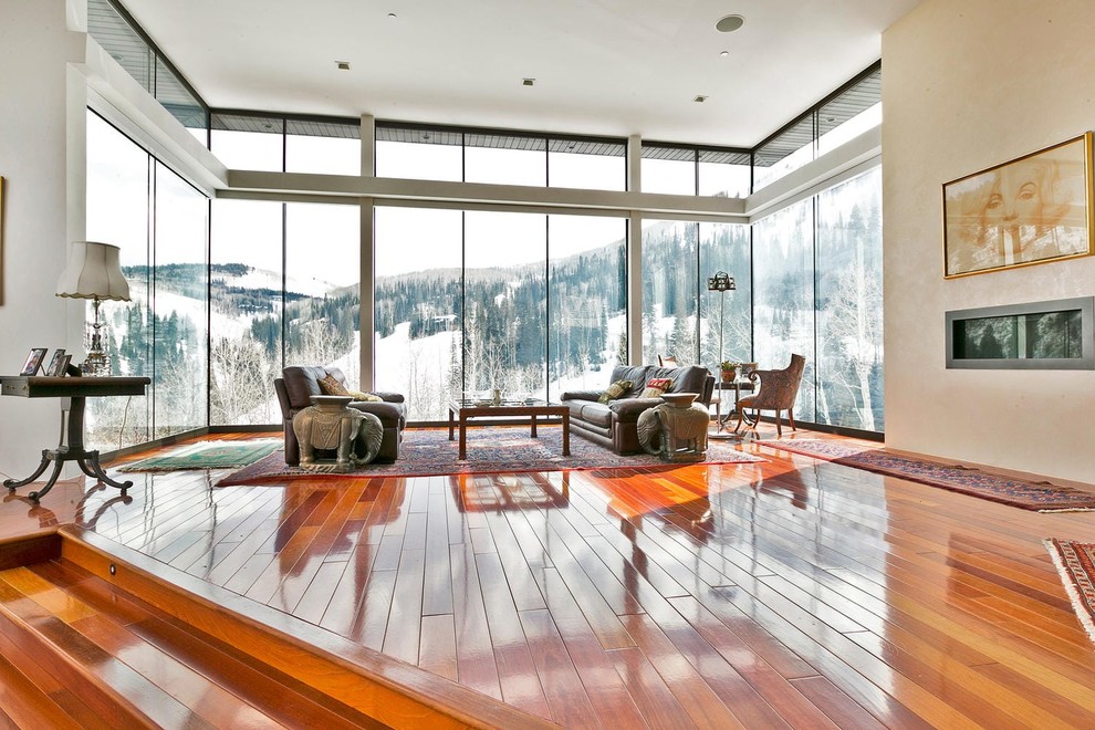 Modelo de salón abierto actual con paredes beige, suelo de madera en tonos medios, chimenea lineal y suelo naranja