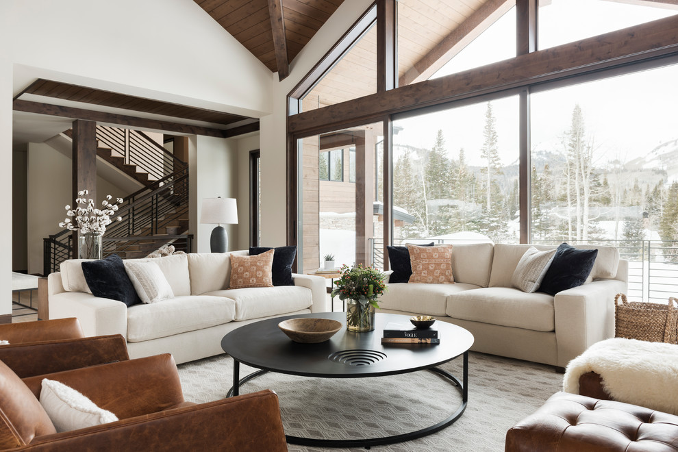 Cette image montre un grand salon design ouvert avec un bar de salon, un mur beige, un sol en bois brun, une cheminée standard, un manteau de cheminée en pierre, un sol beige et éclairage.