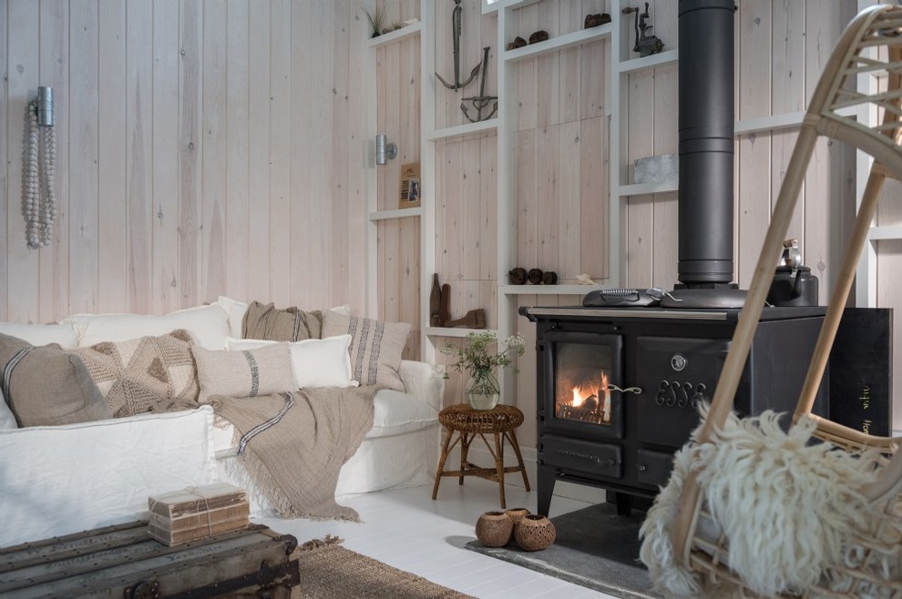 Abgetrenntes Landhausstil Wohnzimmer mit beiger Wandfarbe, gebeiztem Holzboden, Kaminofen, Kaminumrandung aus Metall und weißem Boden in Cornwall