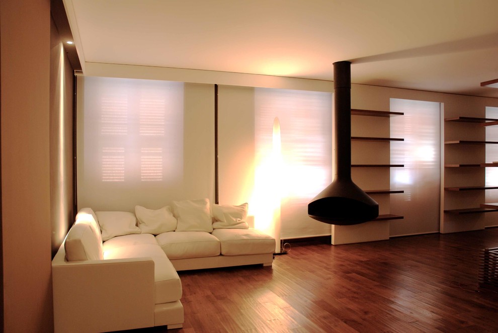 Cette image montre un petit salon minimaliste ouvert avec une bibliothèque ou un coin lecture, un mur blanc, parquet foncé, cheminée suspendue, un manteau de cheminée en métal et un téléviseur indépendant.