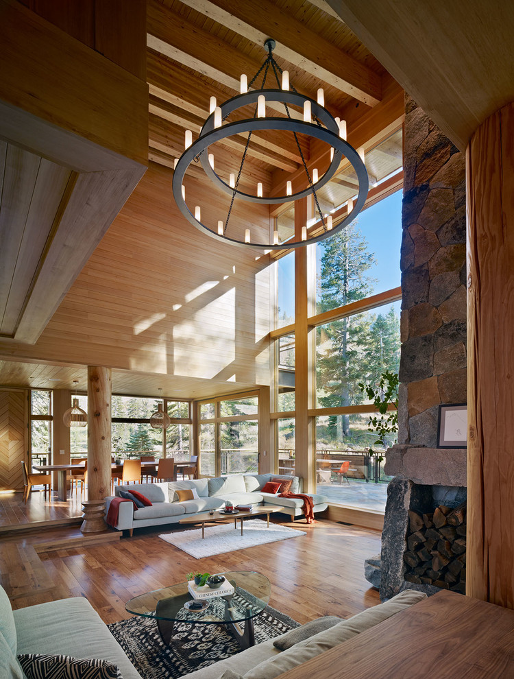 Exemple d'un grand salon montagne ouvert avec un sol en bois brun, une cheminée d'angle et un manteau de cheminée en pierre.