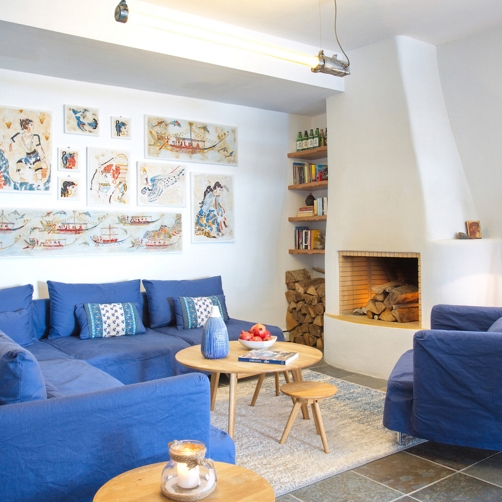 На фото: гостиная комната в средиземноморском стиле с белыми стенами, стандартным камином и синим диваном