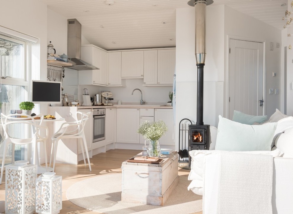 Small beach style open plan living room in Cornwall with white walls, light hardwood flooring, a standard fireplace, a metal fireplace surround, a wall mounted tv and beige floors.