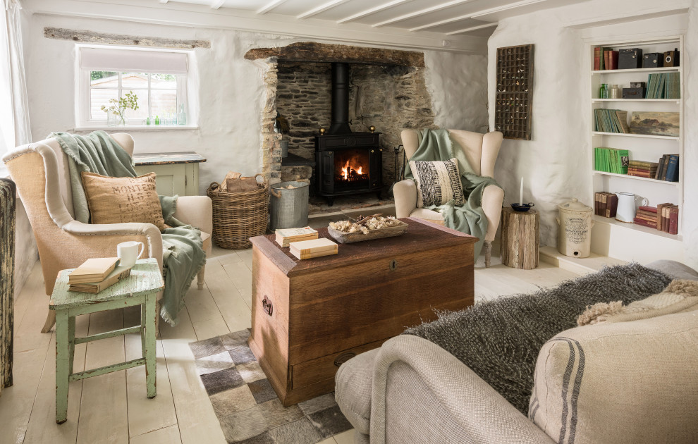 Mittelgroßes Shabby-Look Wohnzimmer mit weißer Wandfarbe, gebeiztem Holzboden, Kamin, Kaminumrandung aus Stein und weißem Boden in Cornwall