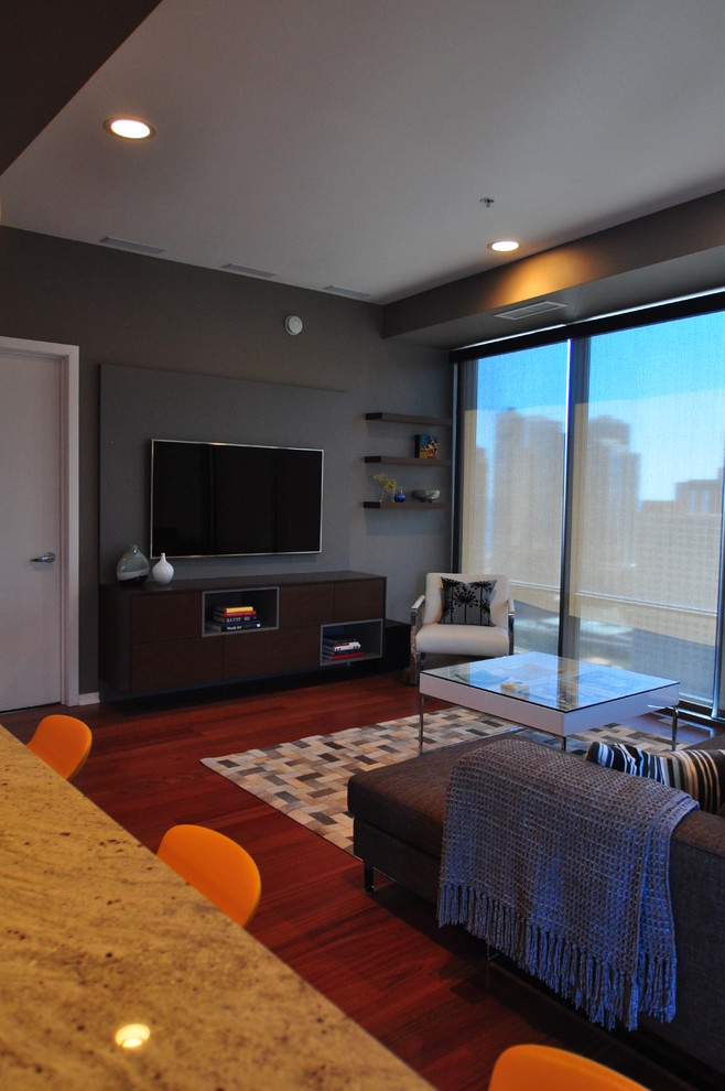 Ejemplo de salón abierto actual grande con paredes grises, suelo de madera en tonos medios y televisor colgado en la pared