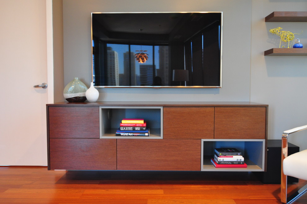 Imagen de salón abierto contemporáneo grande con paredes grises, suelo de madera en tonos medios y televisor colgado en la pared